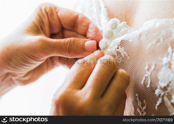 A Bridesmaid helping bride fasten corset and getting her dress, preparing bride in morning for the wedding day