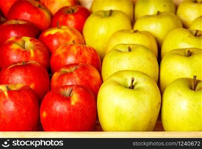 A bright background of fresh apples in red and yellow that are laid out in even rows on a market counter and attracts attention. Focus on foreground, background in slight blur.. Juicy apple background from red and yellow apples for sale in the market, close-up.
