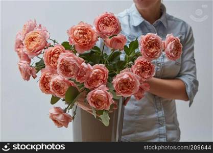 A bright bouquet of fresh pink roses in a vase. The girl is holding a flowerpot on a gray background in her hands. A gift for Valentine&rsquo;s Day. A bouquet of fresh pink roses in a brown vase holds a girl in her hands