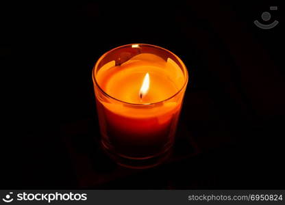 A bright orange candle in a glass candlestick, burning in the dark