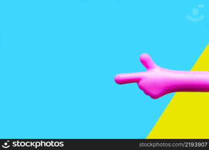 a bright pink plastic hand pointing with the index finger against a yellow-blue background. copy space.
