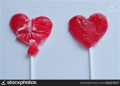 A broken red heart lollipop and a whole one symbolizing a relationship were one partner is heart broken