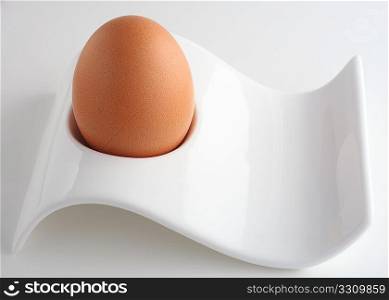 A brown egg in a modern-style eggcup, viewed from the side,with a light shadow