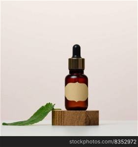 A brown glass bottle with a paper label and a pipette on a white table. Containers for cosmetics, oils and essences