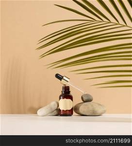 a brown glass bottle with a pipette and a brown label stands on a stone. Container for cosmetics, serum and oil. Palm leaf shadow