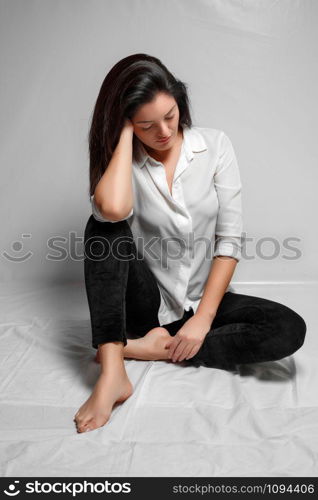 a brunette woman in a white shirt and black leggings sits on a white background