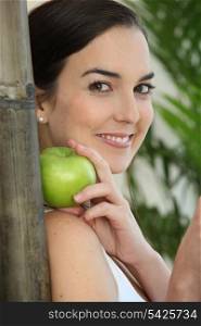 a brunette woman with an apple leaning against a bamboo stick