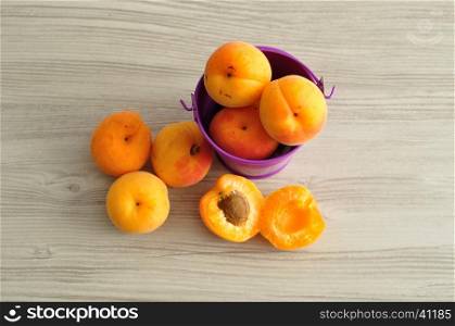 A bucket filled with apricots and two lose ones next to it. Top view.