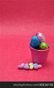 A bucket filled with easter eggs and some small ones laying next to it