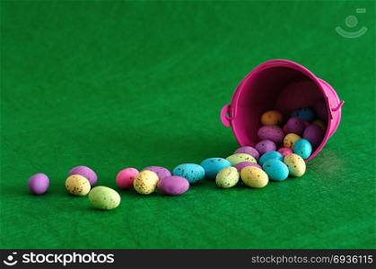 A bucket with easter eggs spilling out on to a green background