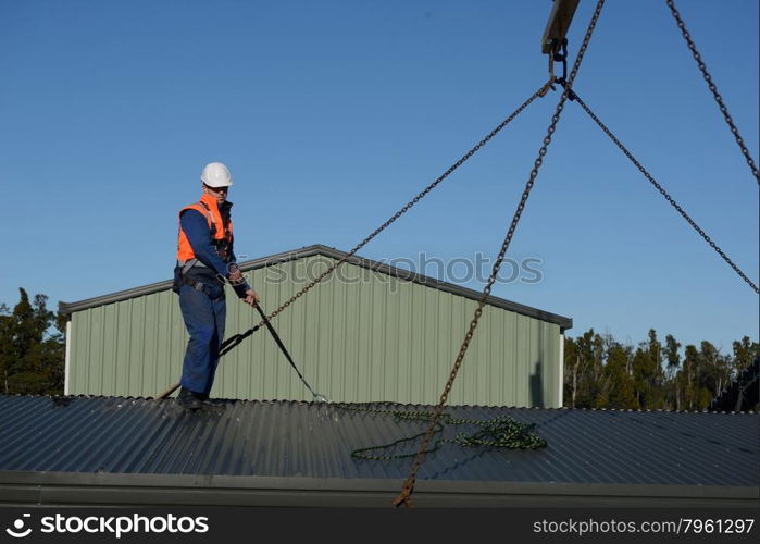A builder wearing a safety harness helps to place the sling in place for a crane to lift a portable building