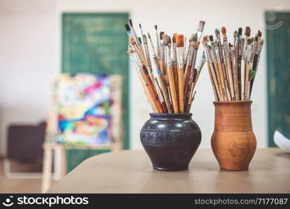 A bunch of art brushes standing in ceramic vases, on the table in the art studio.. A bunch of art brushes standing in ceramic vases, on the table in the art studio