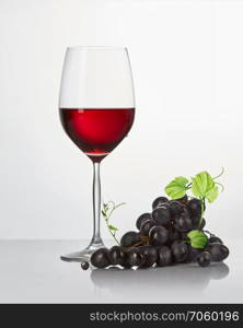 a bunch of blue vines and a glass of red wine on a white background. Red wine in a glass isolated