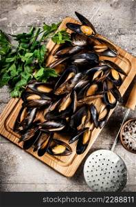 A bunch of boiled mussels on a wooden cutting board. On a gray background. High quality photo. A bunch of boiled mussels on a wooden cutting board.