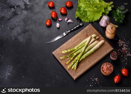 A bunch of branches of fresh green raw asparagus on a wooden cutting board against a dark concrete background. A bunch of branches of fresh green raw asparagus on a wooden cutting board