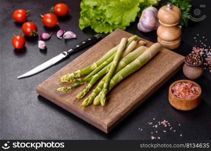 A bunch of branches of fresh green raw asparagus on a wooden cutting board against a dark concrete background. A bunch of branches of fresh green raw asparagus on a wooden cutting board