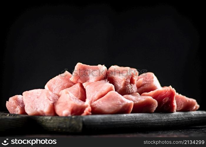 A bunch of chopped raw pork on a cutting board. On a black background. High quality photo. A bunch of chopped raw pork on a cutting board.