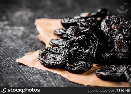 A bunch of delicious prunes on paper on the table. On a black background. High quality photo. A bunch of delicious prunes on paper on the table.
