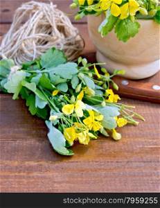 A bunch of flowers celandine on the table, ball of twine, a knife, a wooden mortar in the background of wooden boards