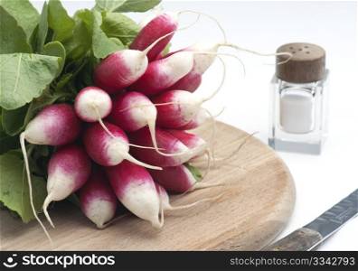 A Bunch Of Fresh French Breakfast Radish On A Wooden Chopping Board, With A Salt Pot and knife, On A White Background