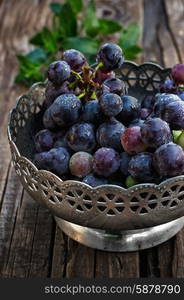 A bunch of grapes. Brush ripe and juicy grapes in vintage iron vase on wooden background