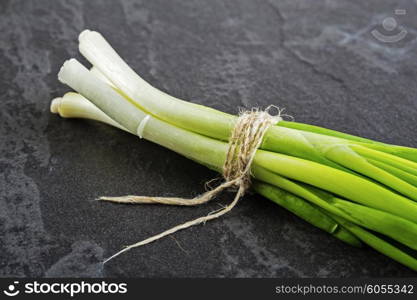 A bunch of green onions on a black stone table