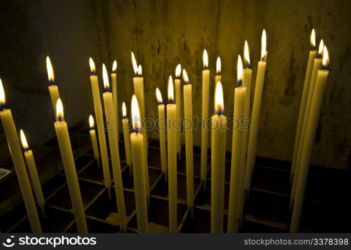 a bunch of long candles in an old dark church