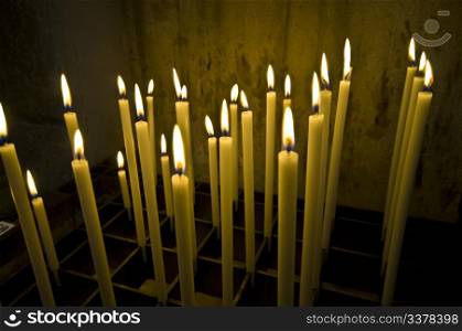 a bunch of long candles in an old dark church