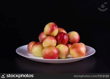 a bunch of ripe nectarines lie on a large white plate background black, close-up. a bunch of nectarines