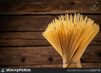 A bunch of spaghetti dry tied with a rope. On a wooden background. High quality photo. A bunch of spaghetti dry tied with a rope.
