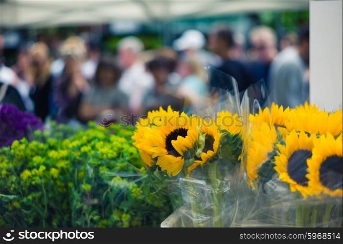A bunch of sunflowers at a flower market with people in the background