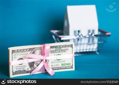 a bundle of dollars tied with a pink ribbon on against the background of a consumer basket with a house. home loan concept