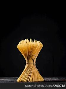 A bundle of spaghetti dry tied with a rope stands on the table. On a black background. High quality photo. A bundle of spaghetti dry tied with a rope stands on the table.