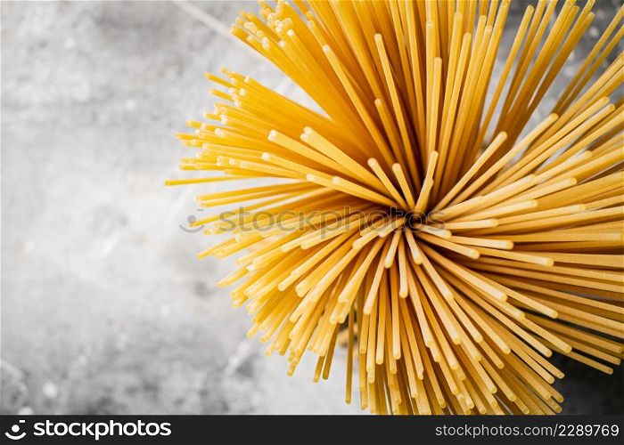 A bundle of spaghetti dry tied with a rope stands on the table. On a gray background. High quality photo. A bundle of spaghetti dry tied with a rope stands on the table.