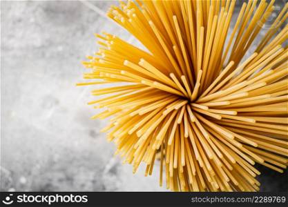 A bundle of spaghetti dry tied with a rope stands on the table. On a gray background. High quality photo. A bundle of spaghetti dry tied with a rope stands on the table.