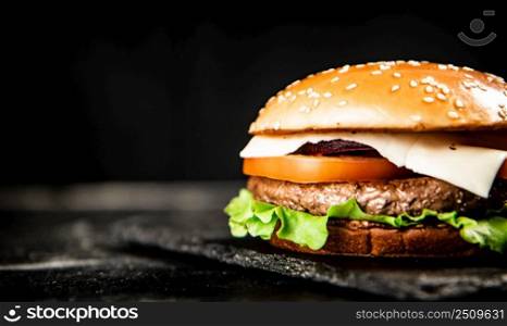 A burger on a stone board on a table. On a black background. High quality photo. A burger on a stone board on a table. 
