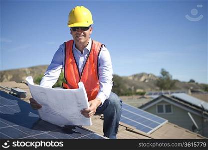 A business man on a solar panalled rooftop looking at plans