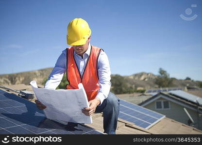 A business man on a solar panalled rooftop looking at plans