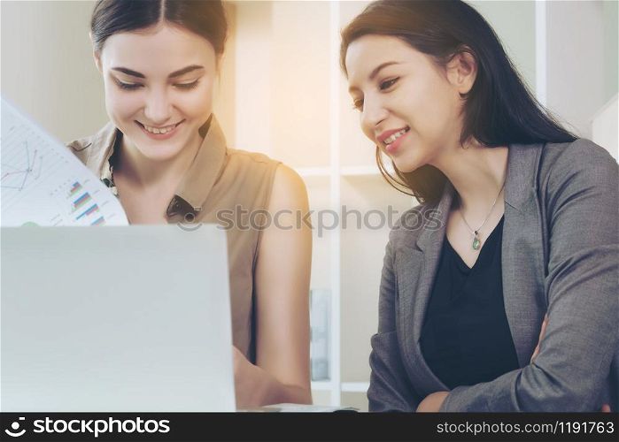 A business woman works in office while having a business conversation with another woman. Concept of co-working business partner and friends in workplace.