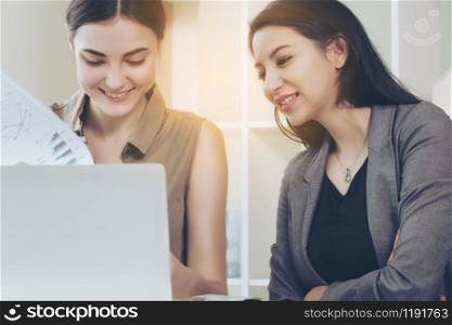 A business woman works in office while having a business conversation with another woman. Concept of co-working business partner and friends in workplace.