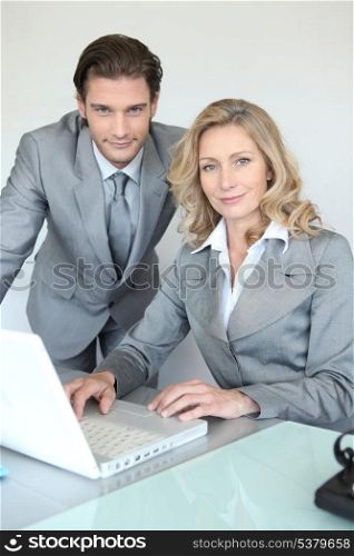 A businessman and a businesswoman working in front of a laptop and looking at us.