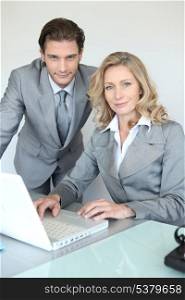 A businessman and a businesswoman working in front of a laptop and looking at us.