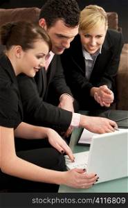 A businessman and his two female colleagues looking at a presentation on a white laptop computer. The focus is on the man in the middle.