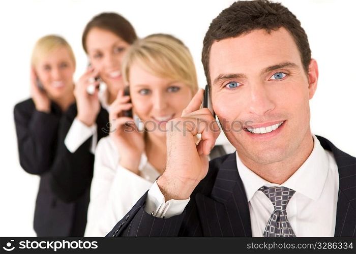 A businessman and three businesswomen out of focus behind him all talking on cell phones