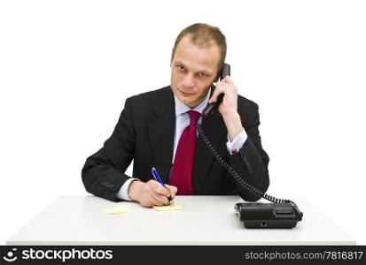 A businessman behind a desk taking notes whilst intentively listening to a client on the phone