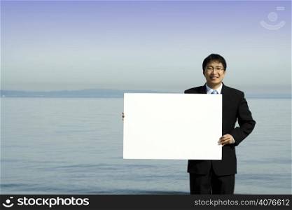 A businessman carrying a blank white board at the beach