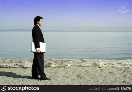 A businessman carrying a laptop at the beach