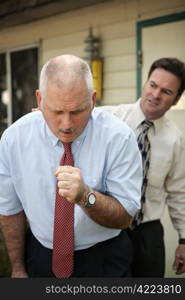 A businessman doubled over in a coughing fit as a coworker looks on.