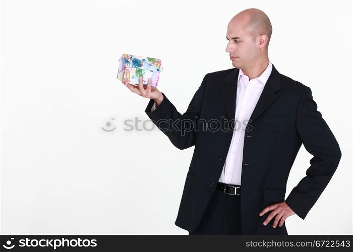 A businessman holding a miniature house made out of bills.