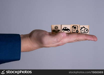 A businessman holds wooden cubes and a hand depicting a house with tax badges and a mortgage on the property. The concept of the Tax Property Law as of the date.. A businessman holds wooden cubes and a hand depicting a house with tax badges and a mortgage on the property.